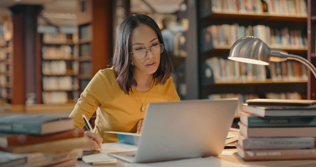 Women researching with books and laptops inside a library. 