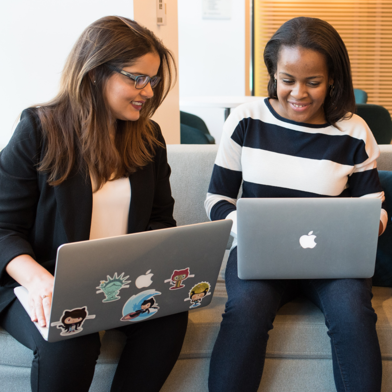 A photo of two people sitting together on a couch, each working on a laptop.