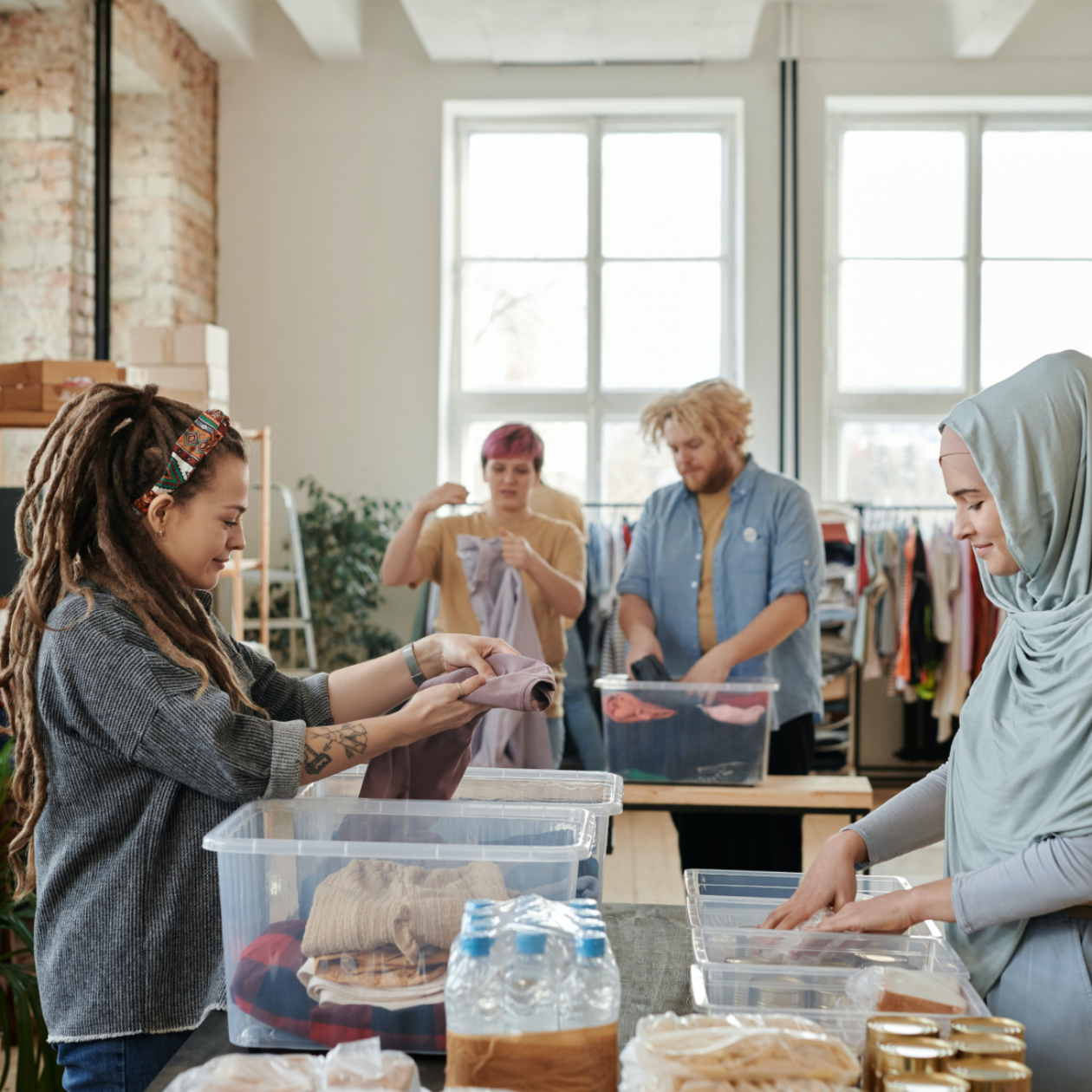 A photo of 4 people sorting clothes and other products into clear bins.