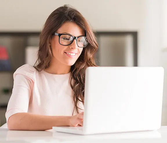 A person is sitting and smiling while working on a laptop.